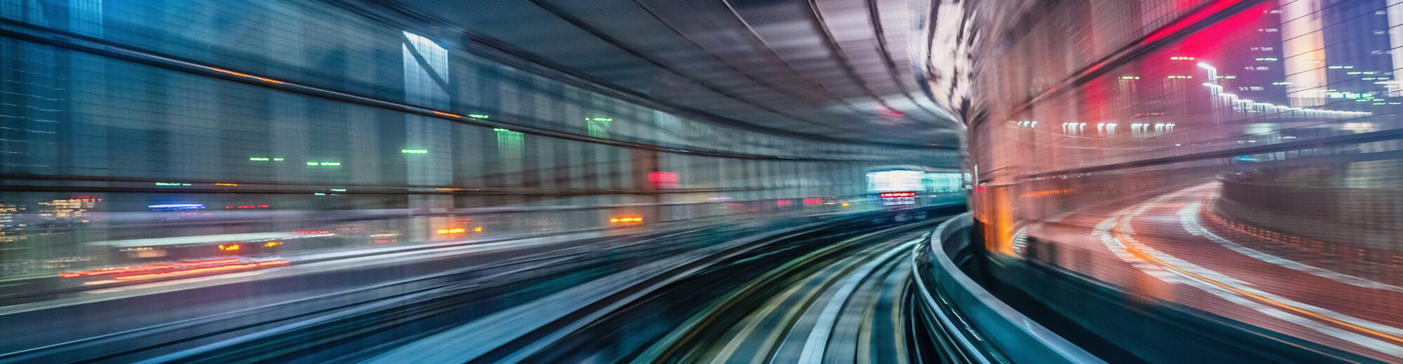 Motion-blurred view from a train speeding through a curved elevated track at night, with glowing city skylines streaking past on both sides.